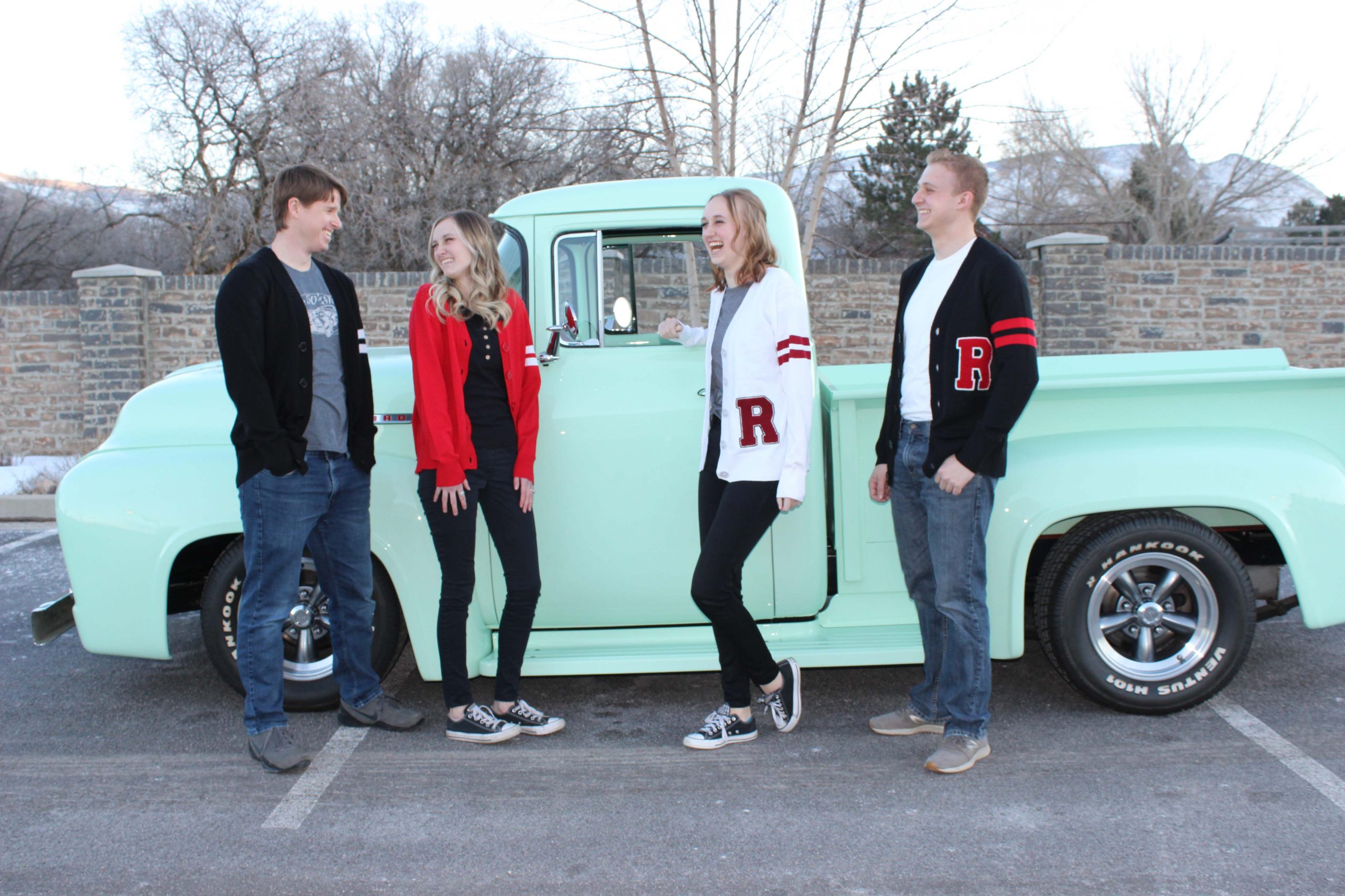 IMG_5015 WOO laughing family siblings spouse standing in front of a 1956 Ford F100 mint green truck modeling vintage style varsity letterman sweaters for men and women with an R monogram over the left pocket in colors black, red and white.