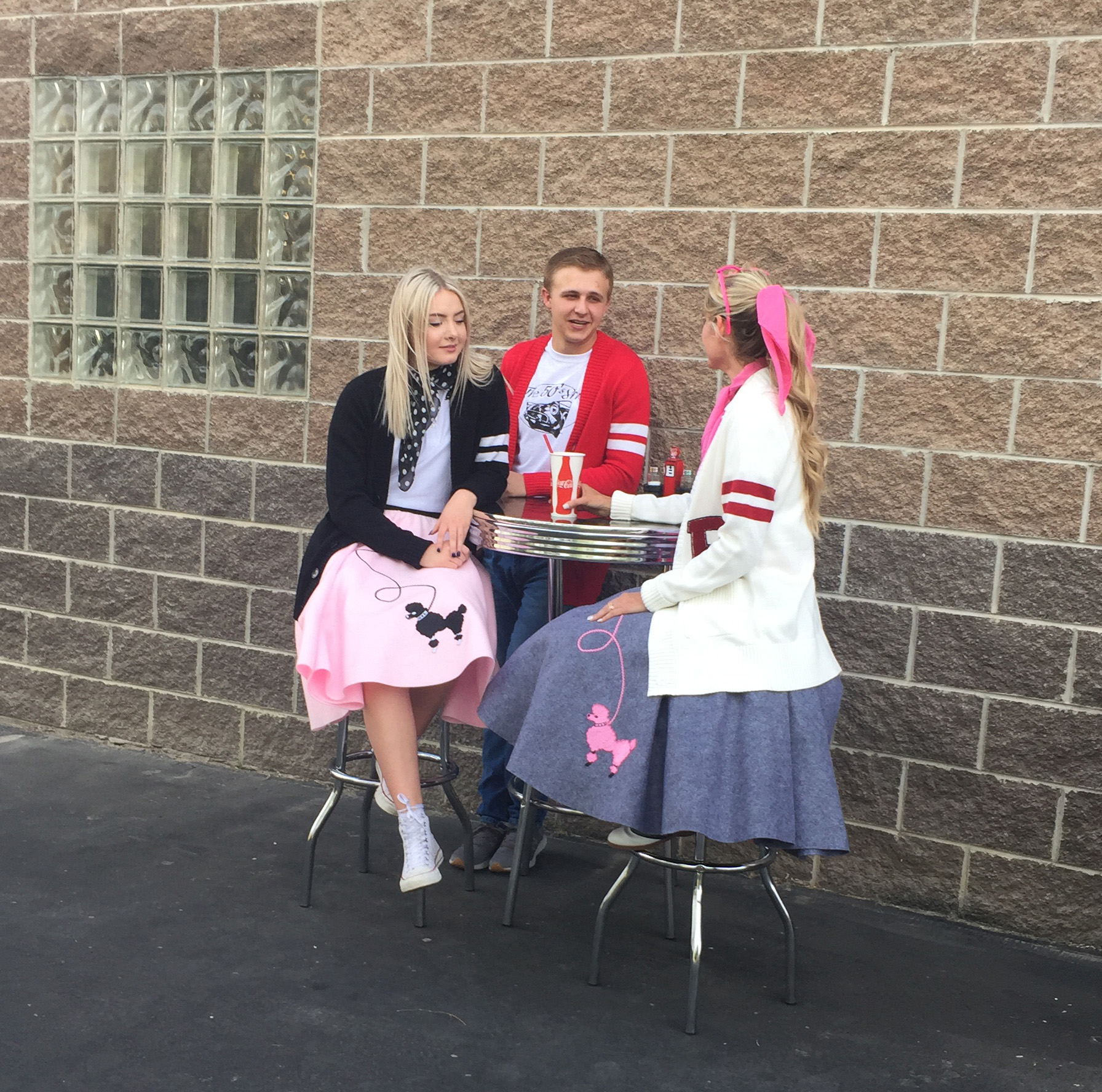 Sweater Lifestyle Sitting 2 Friends sitting at a soda-shop style table wearing vintage poodle skirt outfits and 1950s varsity letterman sweaters drinking soda with converse shoes.