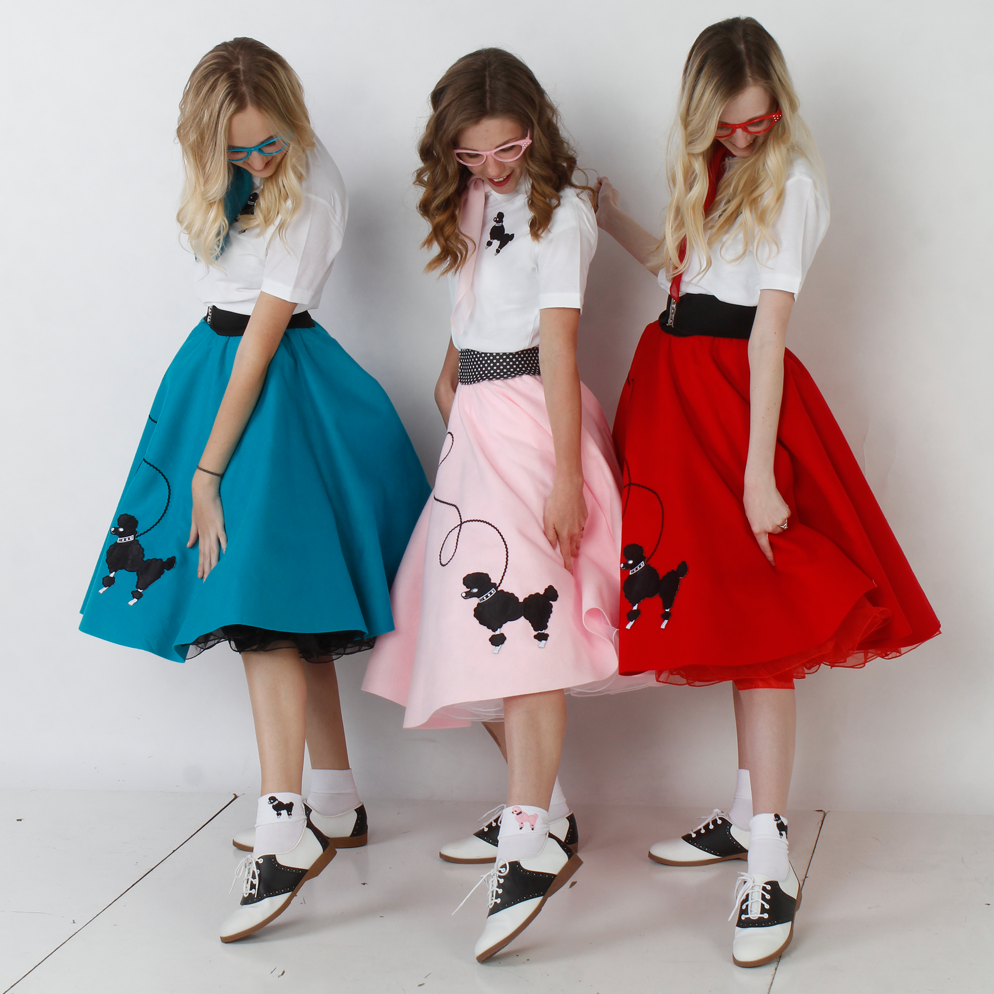 three women wearing poodle skirt outfits, one teal, one light pink, and one red, pointing their shoes to show off their bobby socks