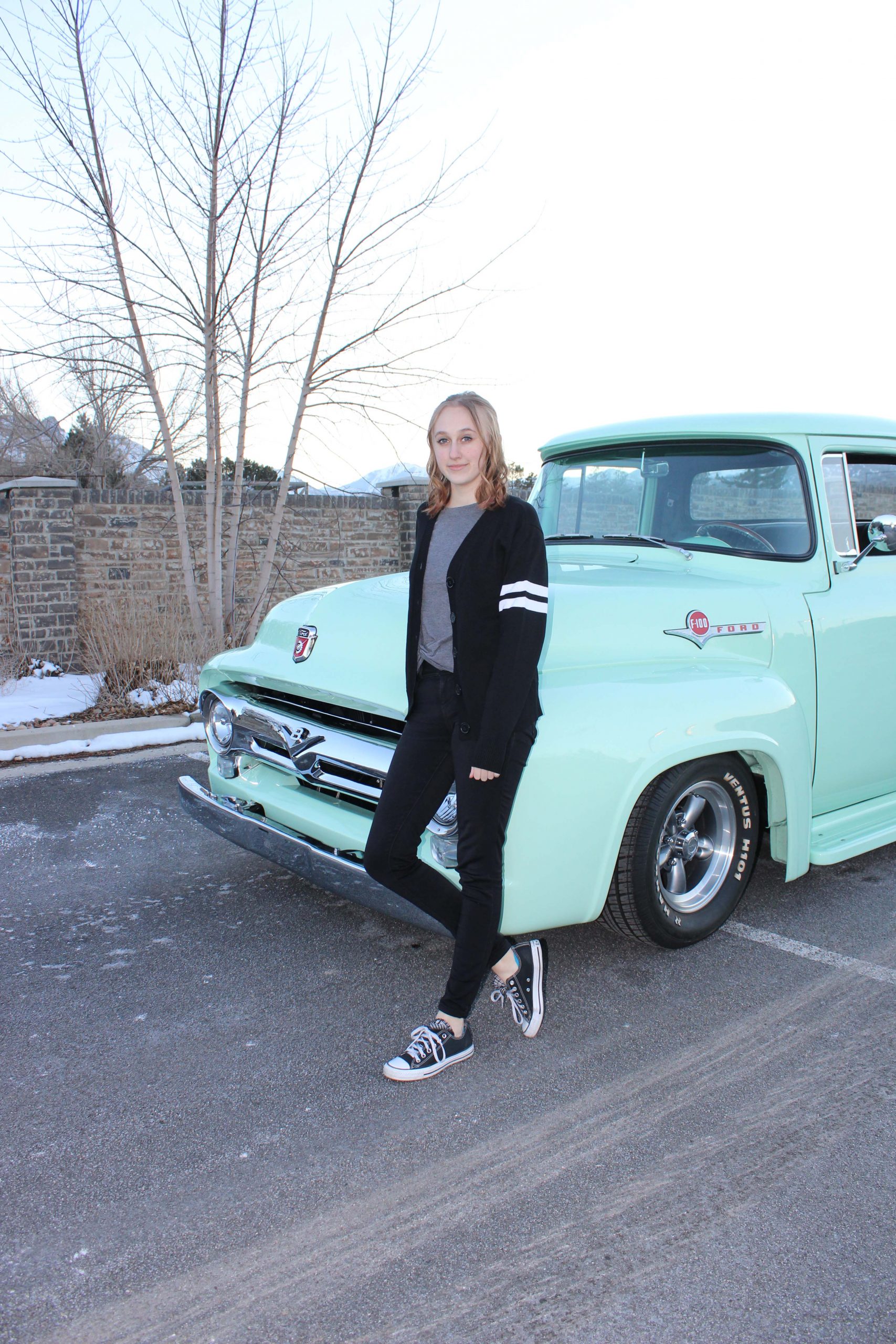 IMG_5081 WOO Girl standing in front of a 1956 Ford F100 Mind Green Truck wearing a black with white stripes varsity letterman sweater with pockets.