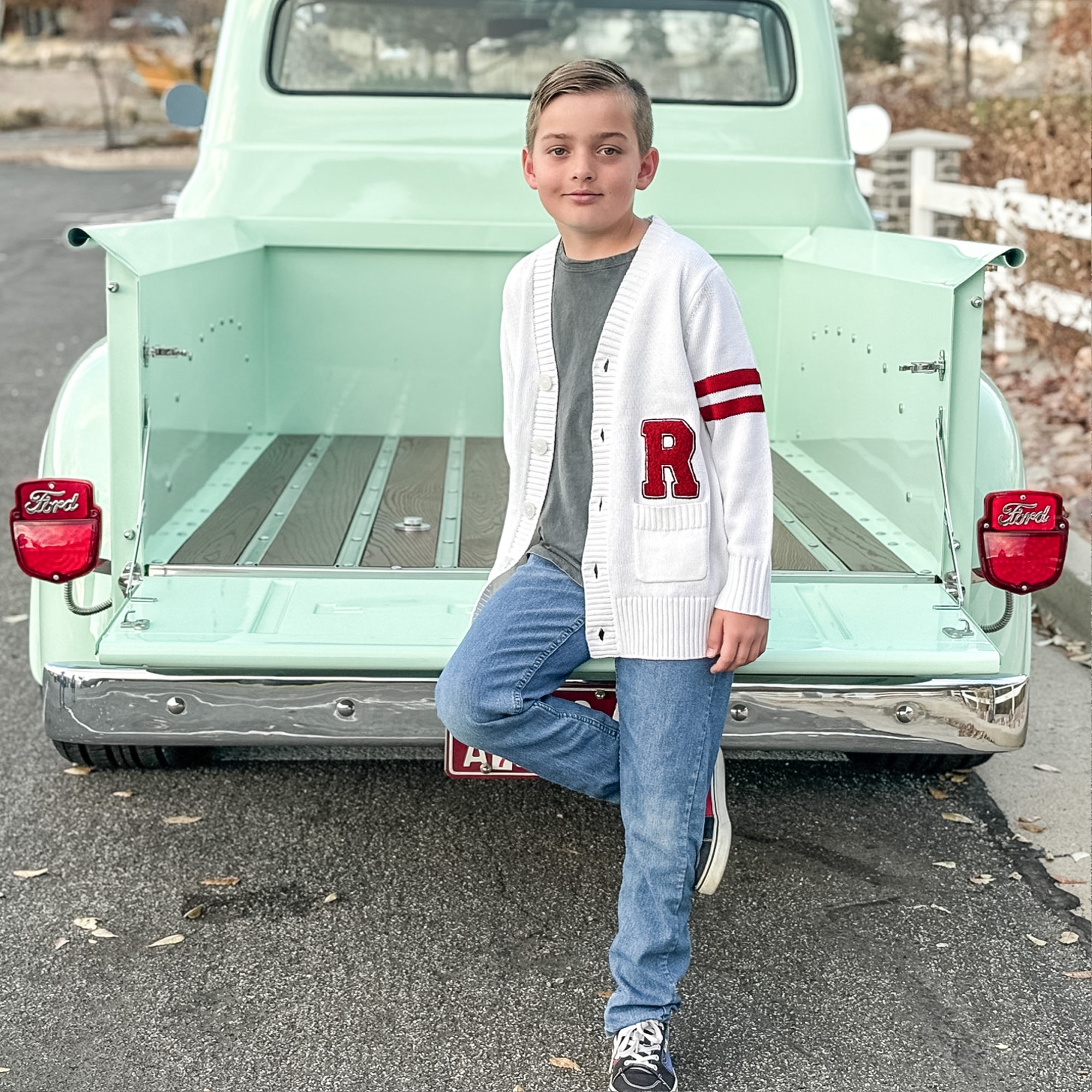 Boy standing in front of a mint colored 1956 Ford F100 Truck modeling a retro letterman sweater with an R monogram.