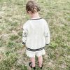 Girl modeling a taylor tot off-white cardigan sweater with three silver embroidered stars on each elbow.