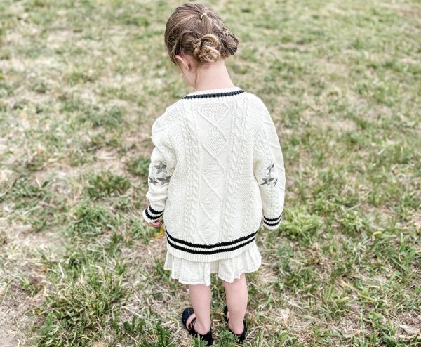 Girl modeling a taylor tot off-white cardigan sweater with three silver embroidered stars on each elbow.