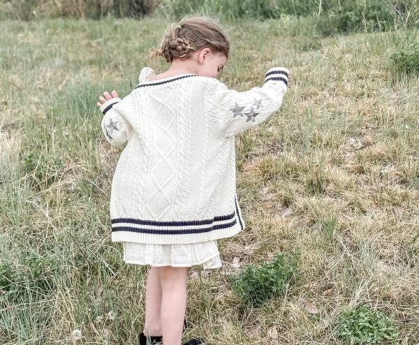 Girls standing in a grassy field wearing a Taylor Tot off-white cardigan sweater with three silver embroidered starts on the sleeve.