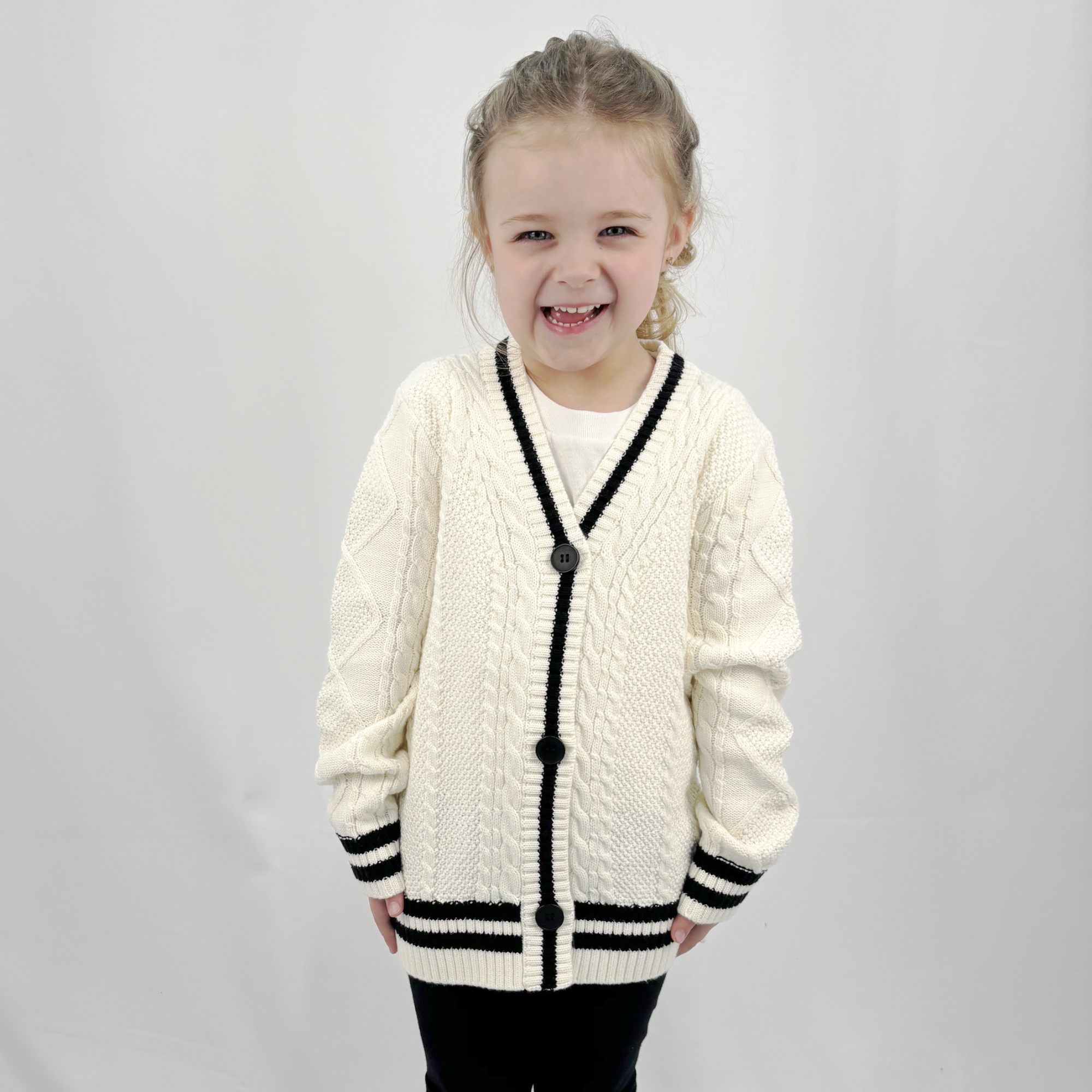 Girl wearing a taylor tot off-white cardigan sweater. Off white with black stripe and 3 buttons.