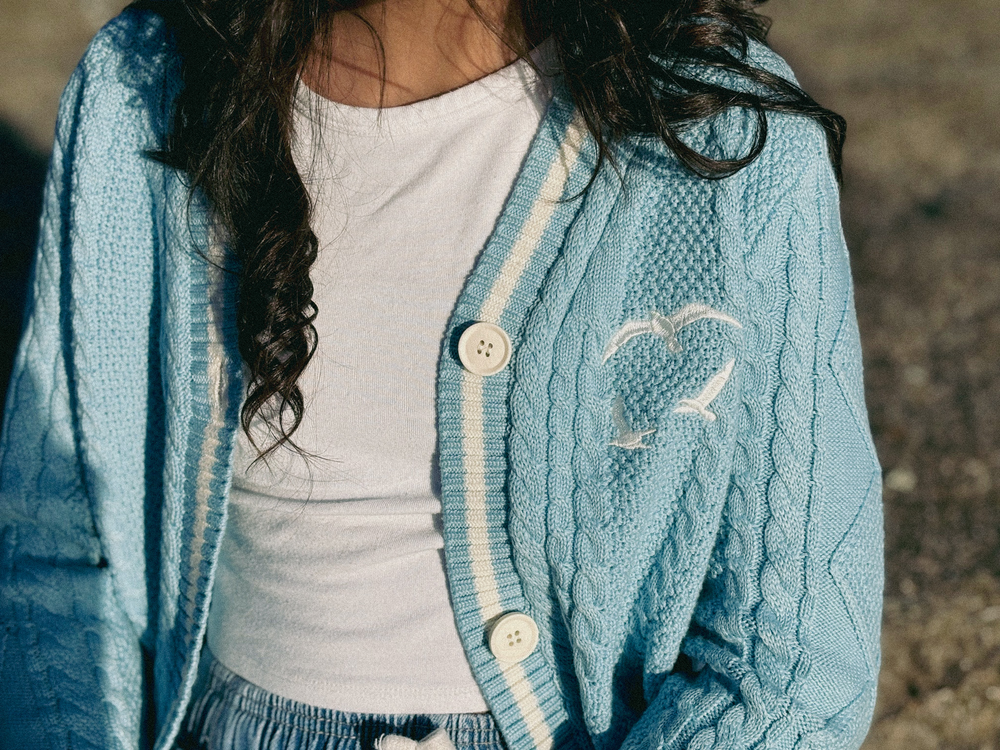 little girl wearing blue cardigan with white stripes and buttons and seagulls on the chest